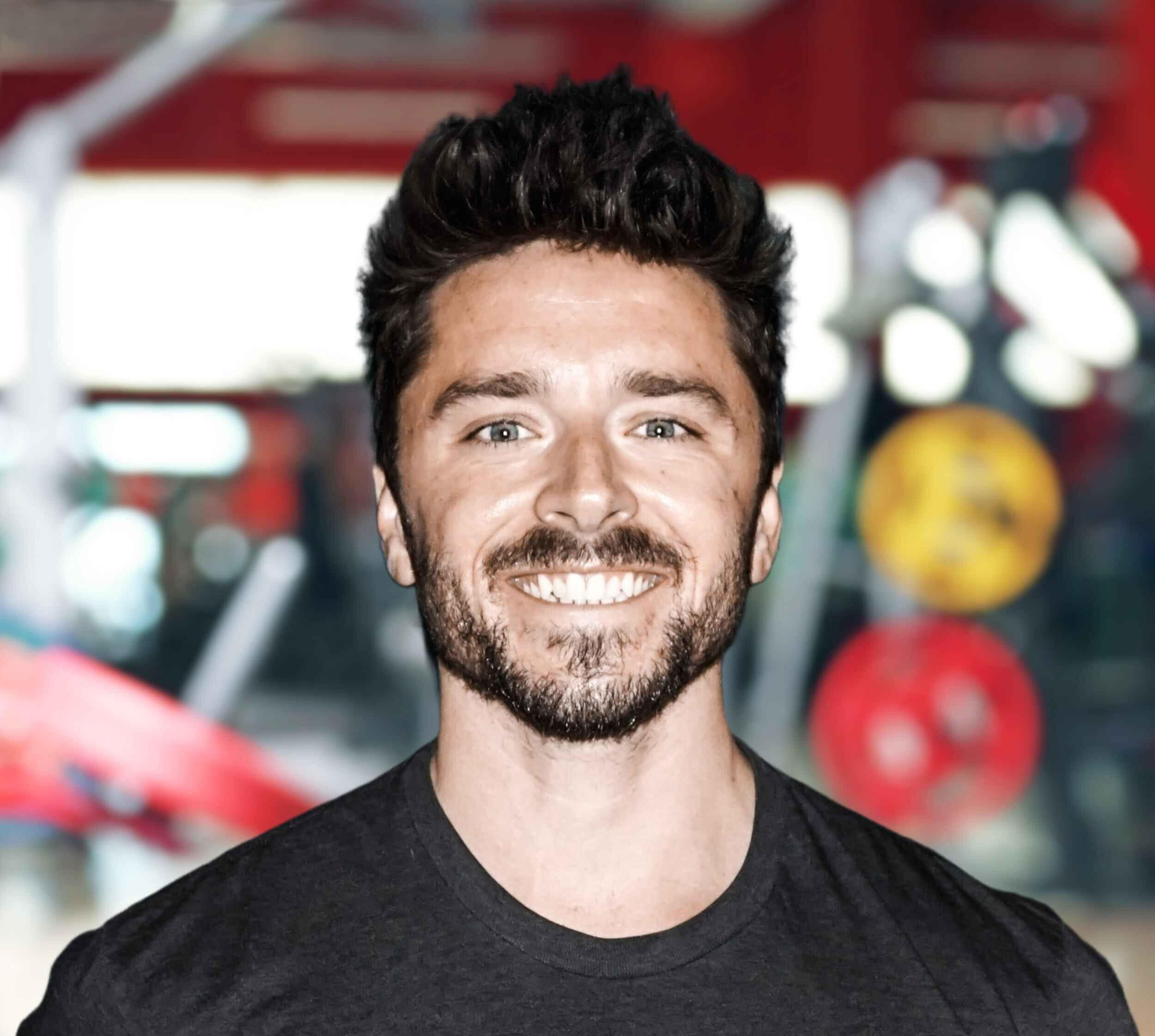 Kyle Olmstead's professional headshot, featuring him in front of a gym background, representing his expertise in fitness and health.