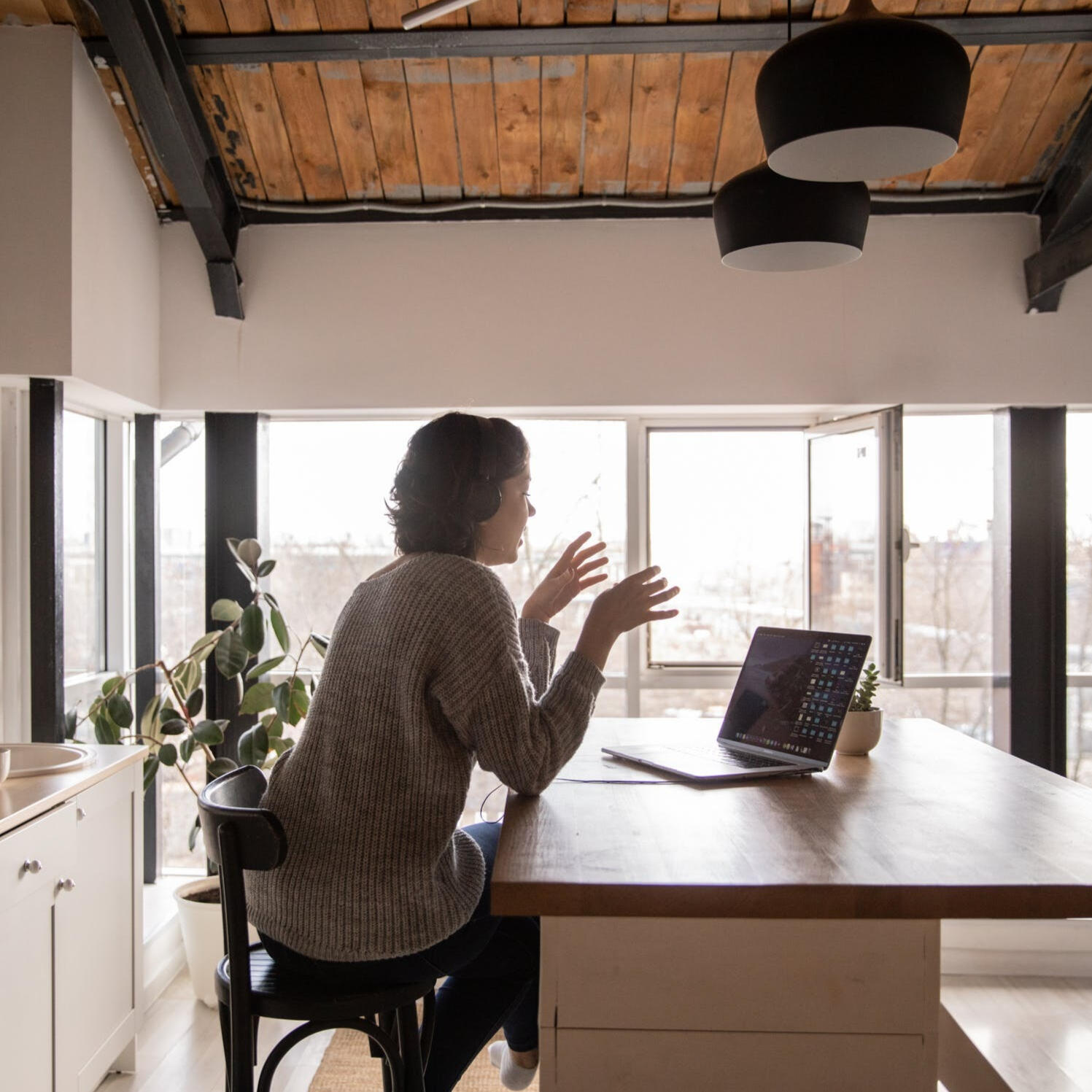 Woman in a stylish kitchen, engaged in a work meeting while talking with her hands at the table, conveying confidence and professionalism.